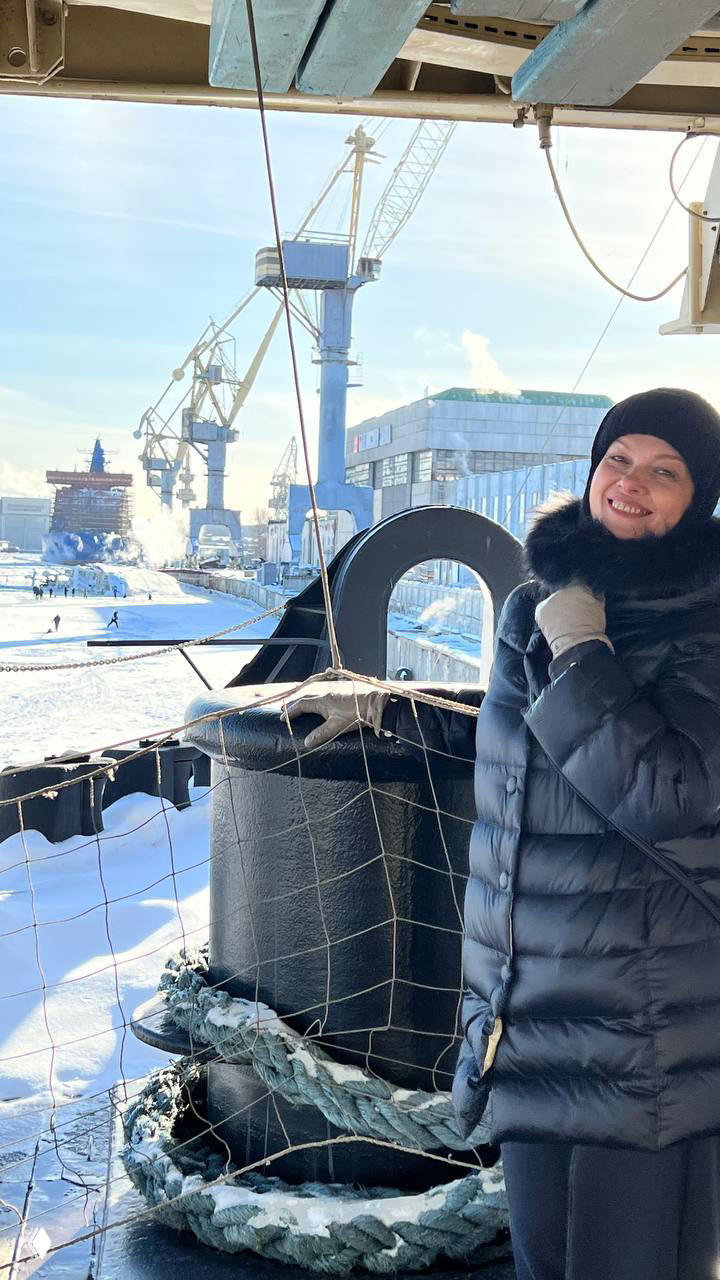 Посетитель на палубе возле швартовного кнехта в зимней одежде; на заднем плане лед и промышленные строения верфей, атмосферный кадр экскурсии.