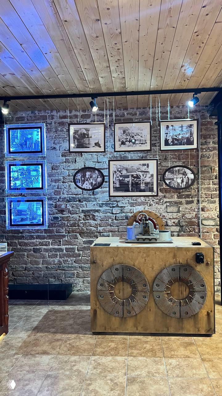 Экспонаты в музее: стенд с старинными фотографиями на кирпичной стене и демонстрационный стол с деревянным оборудованием для бумаги.