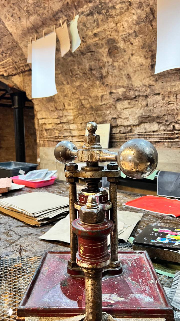 Крупный план старинного ручного пресса или станка для обработки бумаги: металлические детали с налётом времени и следами использования.