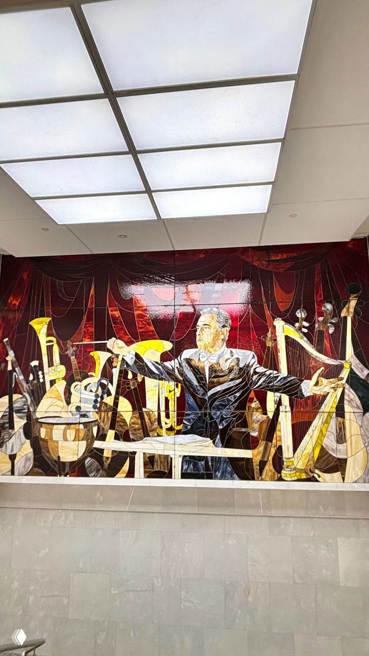 Художественная мозаика или панно с изображением дирижёра и оркестровых инструментов на стене внутри филармонии, крупный план.