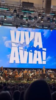 Сцена во время концерта VIVA AVIA: оркестр на сцене и большой экран с яркой надписью VIVA AVIA, вид со зрительного зала.