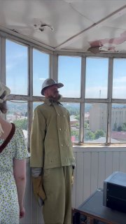 Внутри наблюдательной рубки каланчи: молодая фигура пожарного у окон, вид на город через стекла и панорамная перспектива.