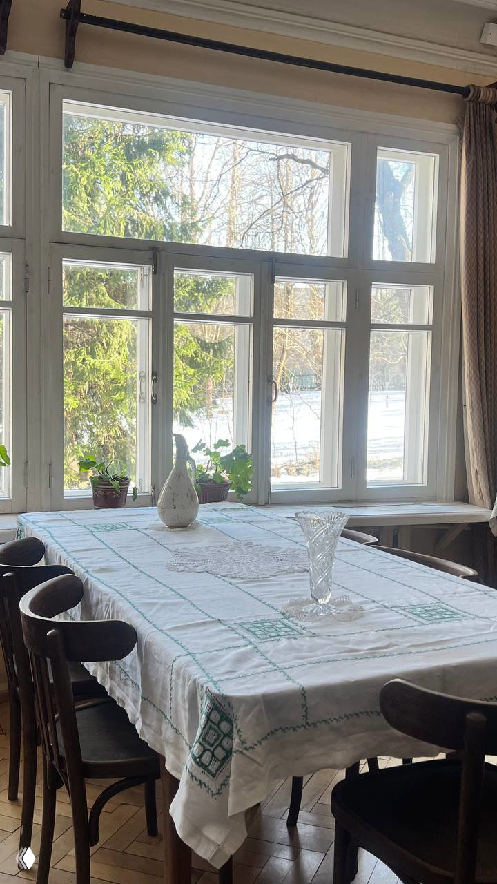 Обеденный стол в доме-музее с вышитой скатертью, вазой и большим окном: вид на сад и свет, затаившийся в комнате для чтения и бесед.