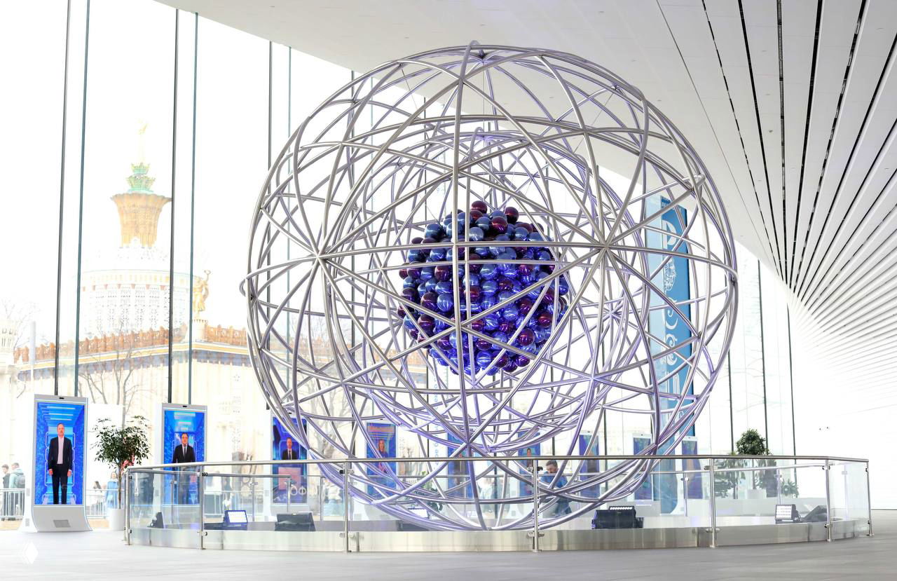 Инсталляция в павильоне «Атом» на ВДНХ: металлическая сферическая конструкция с центральной светящейся композицией на фоне панорамных окон.