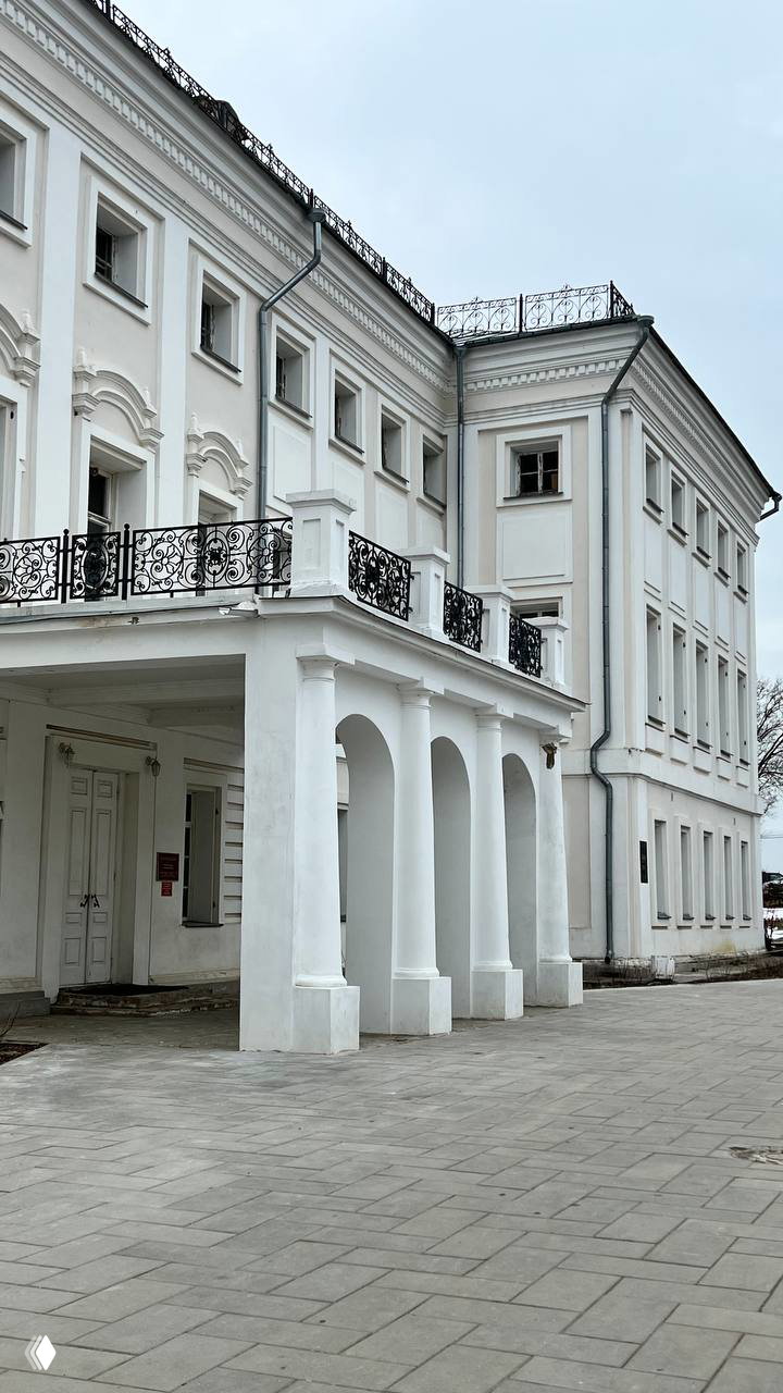 Фасад белого господского дома усадьбы Гончаровых в Полотняном Заводе, фронтальная перспектива колонн и балконов на фоне пасмурного неба