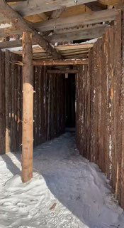 Внутренний проход массивной деревянной инсталляции в Никола-Ленивце зимой, сугробы на полу, высокие столбы и игра света в арт-парке во время Масленицы.