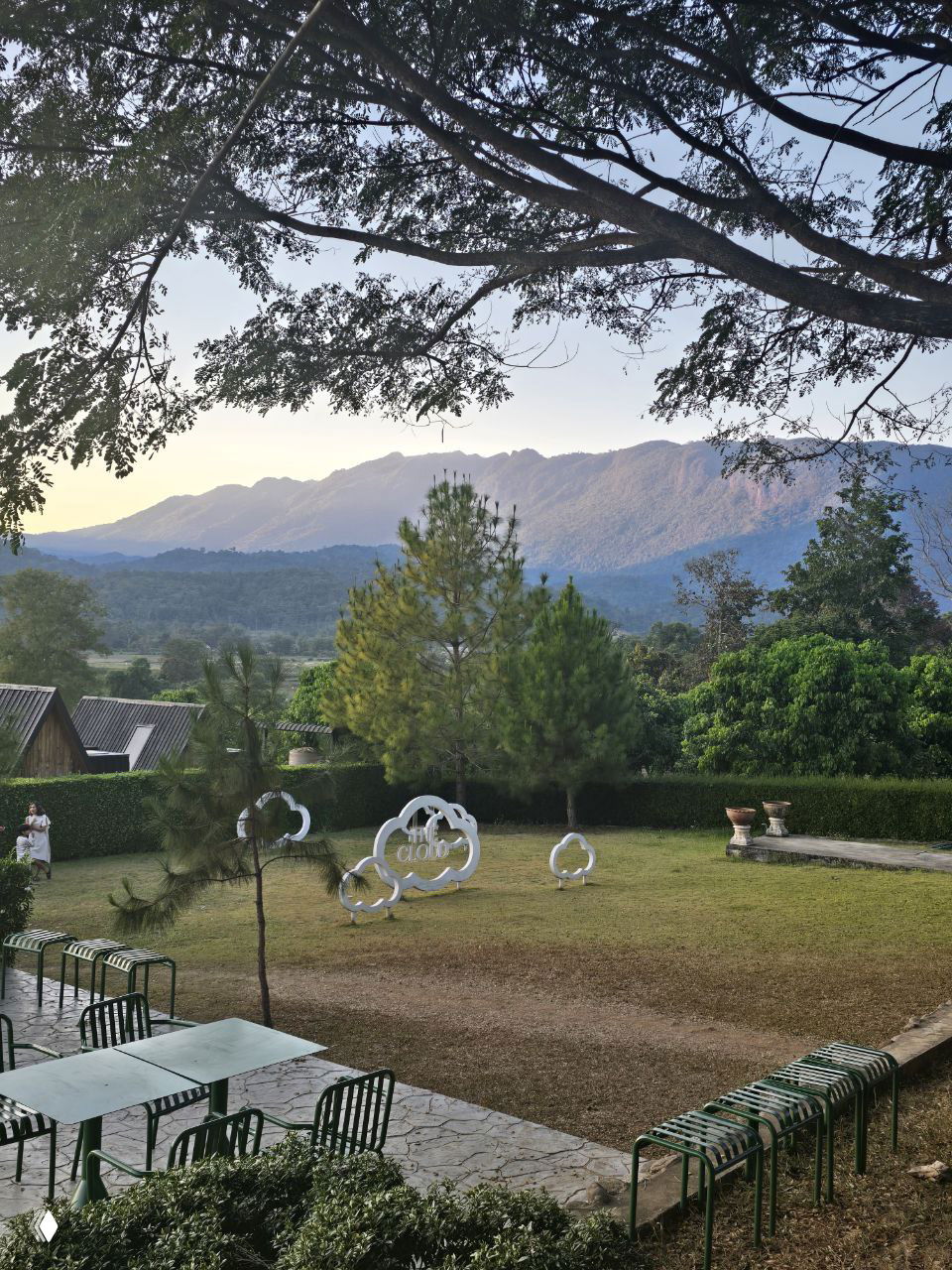 Панорамный вид на горную долину вокруг Чиангмая с деревьями, холмами и зелёными насаждениями; на переднем плане сад и уличные столы для отдыха.