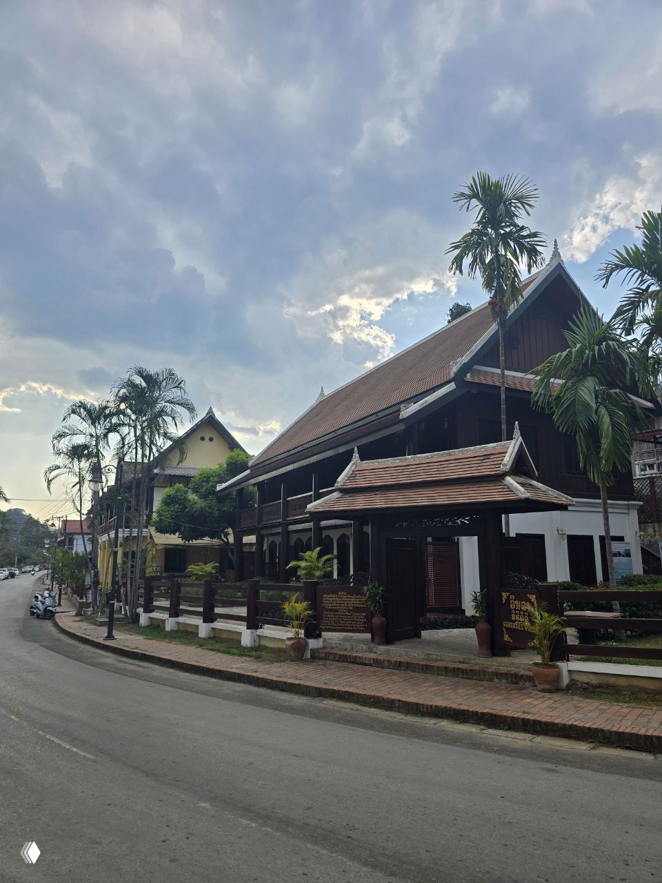 Традиционные лаосские деревянные здания и дома вдоль пустынной улицы, тропические деревья и спокойная атмосфера раннего утра или вечера в туристическом районе.