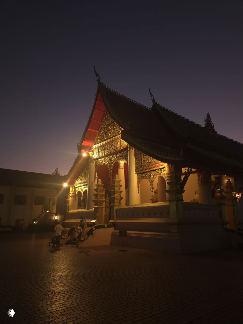 Ночной храм с подсветкой и богато украшенным фасадом, тёплый золотистый свет подчёркивает кровлю и колонны во время сумерек.