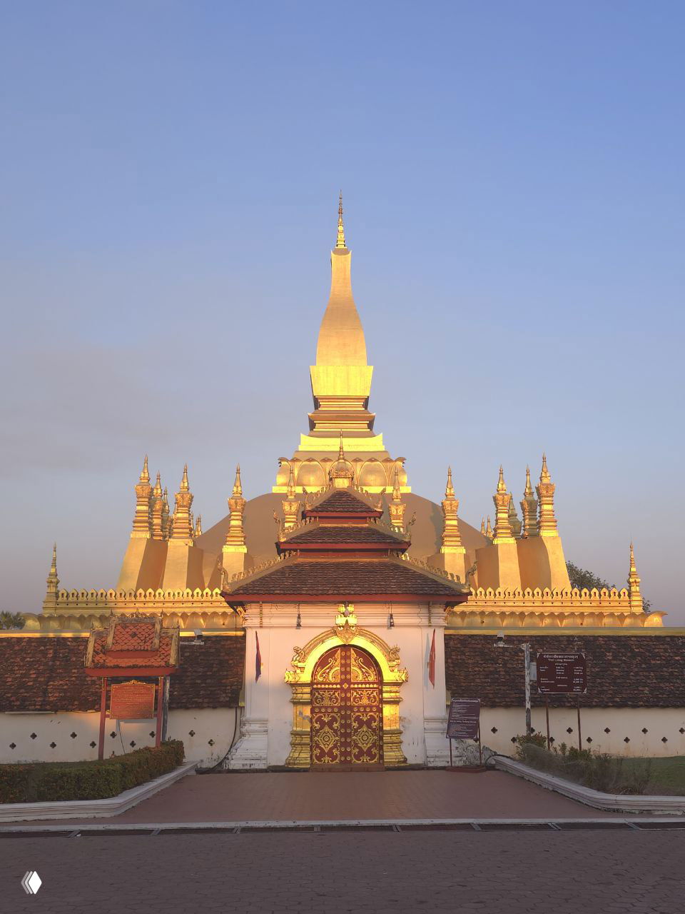 Золотая ступа буддийского храма в Вьентьяне, подсвеченная тёплым светом заката, виден фасад с купольной вершиной и орнаментами.