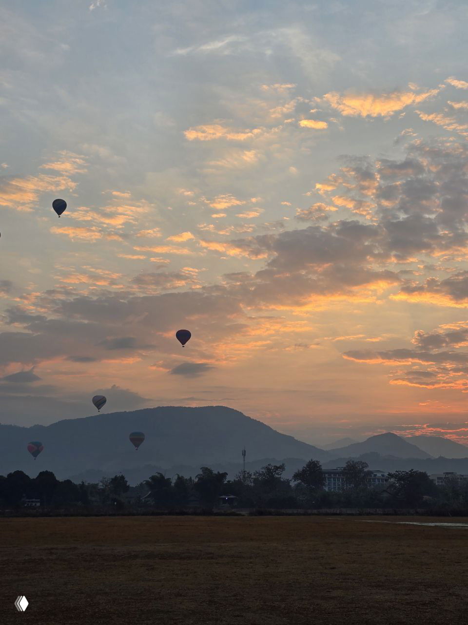 Рассвет над Ванг Вьенгом: десятки воздушных шаров и мотопарапланов поднимаются над силуэтами гор и пастельным небом.