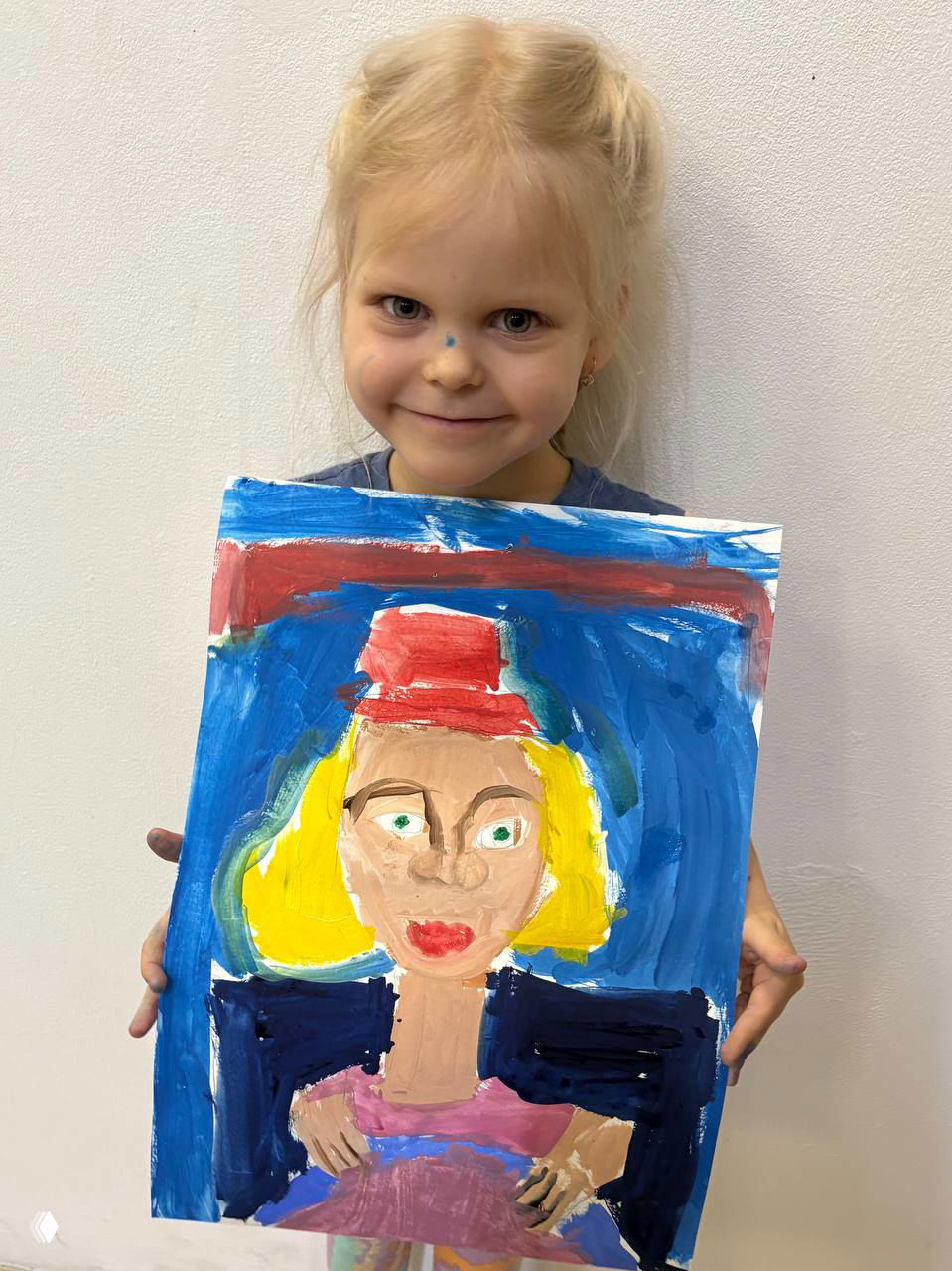 Ребёнок демонстрирует картину женщины с красной шляпой и выразительными глазами, выполненную крупными цветными мазками в наивной манере детского рисунка.