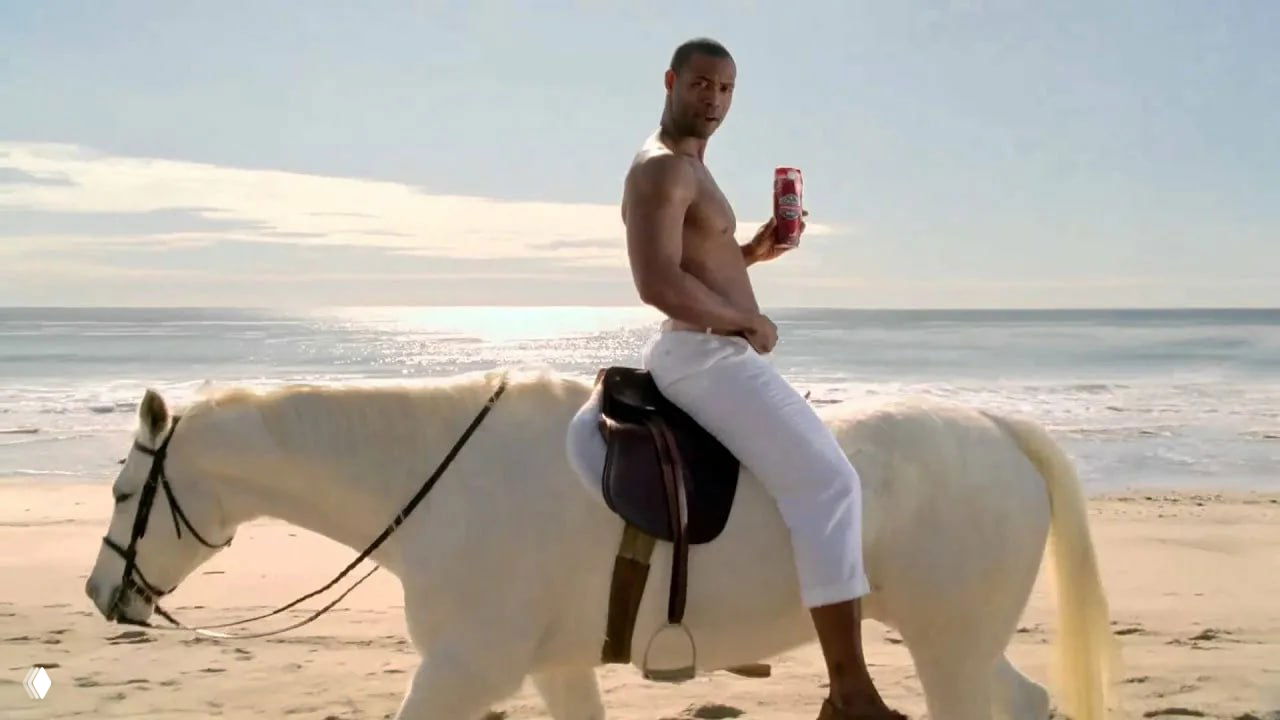 Кадр рекламы Old Spice: мускулистый мужчина верхом на белой лошади на пляже, держит банку продукции — эпатажный, абсурдный ракурс для привлечения внимания.