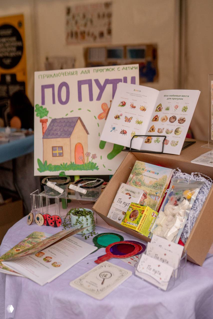 Крупный план стола с продуктами проекта: открытая книга «По пути», коробки с наборами, карточки и печатные материалы для детских прогулок.