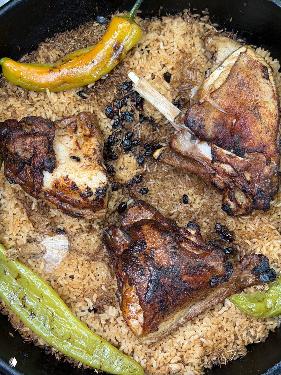 Крупный план плова в казане с золотистым рисом, большими кусками жареного мяса и зелёными перцами — полевой кулинарный момент на фестивале.