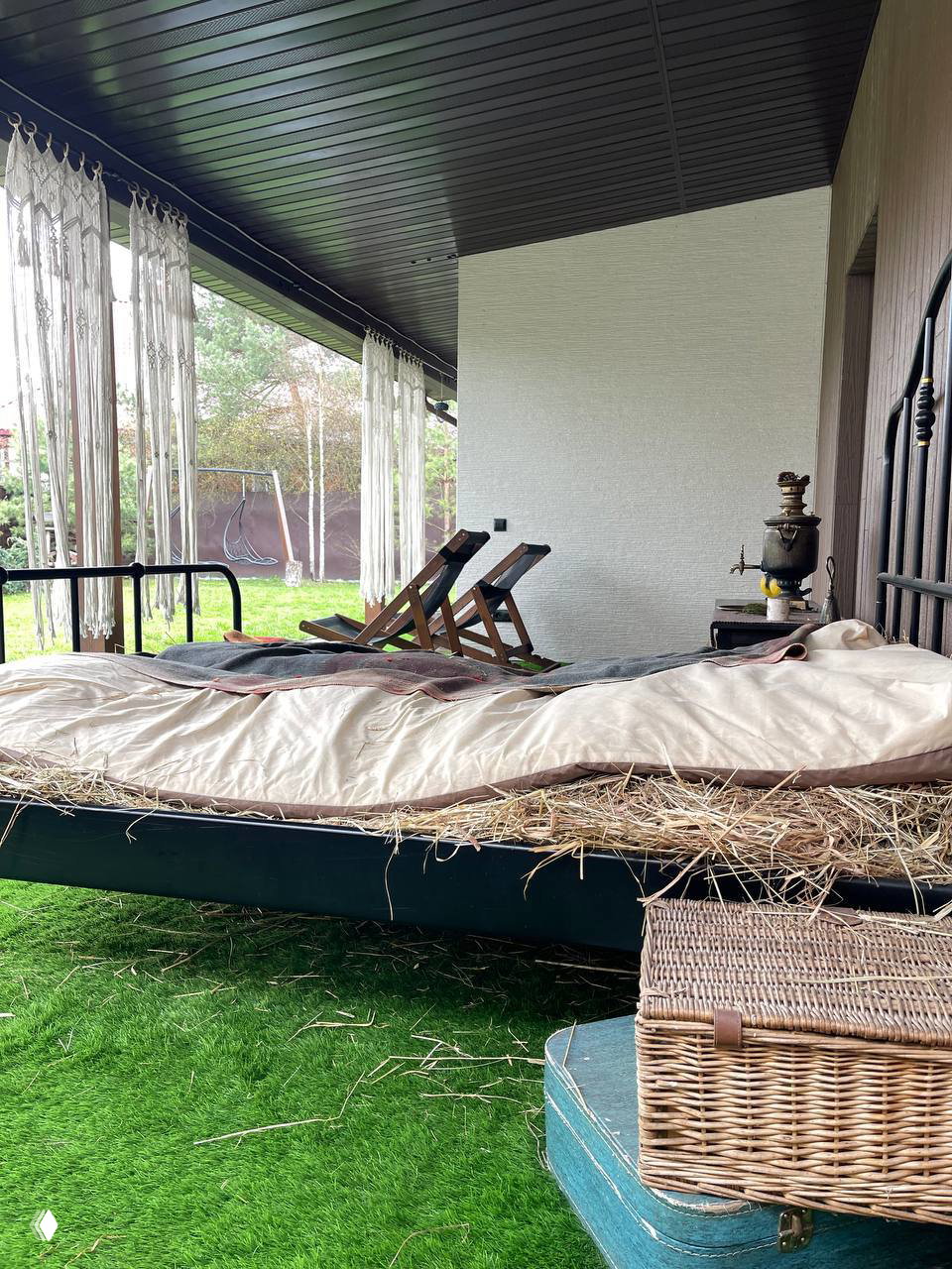 Кровать на веранде, застеленная сеном, с корзиной и чемоданом рядом — расслабляющее место для послебанных снов и отдыха на свежем воздухе.