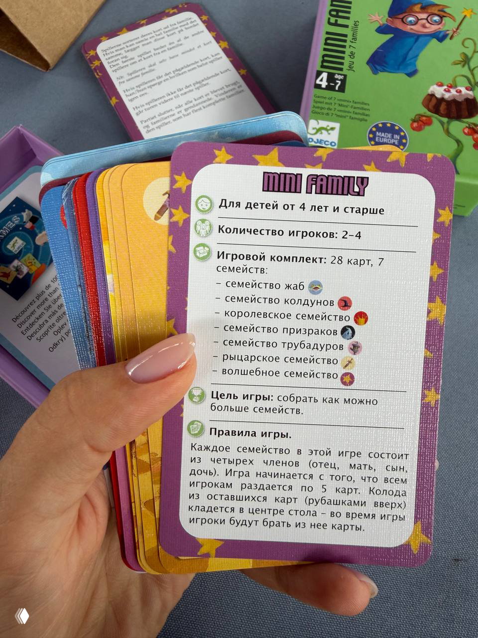Стопка карт игры Mini Family в женской руке: видна карточка с правилами на русском и перечислением семейств игры.