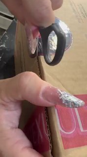 Крупный план рук с длинными декорированными ногтями, держащих чёрный пластиковый компонент на фоне коробки и упаковки товара.