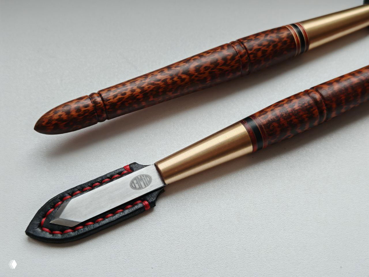Крупный план лезвия и рукояти разметочного ножа: кожаная накладка, шов красной нитью и текстура снейквуда на рукояти