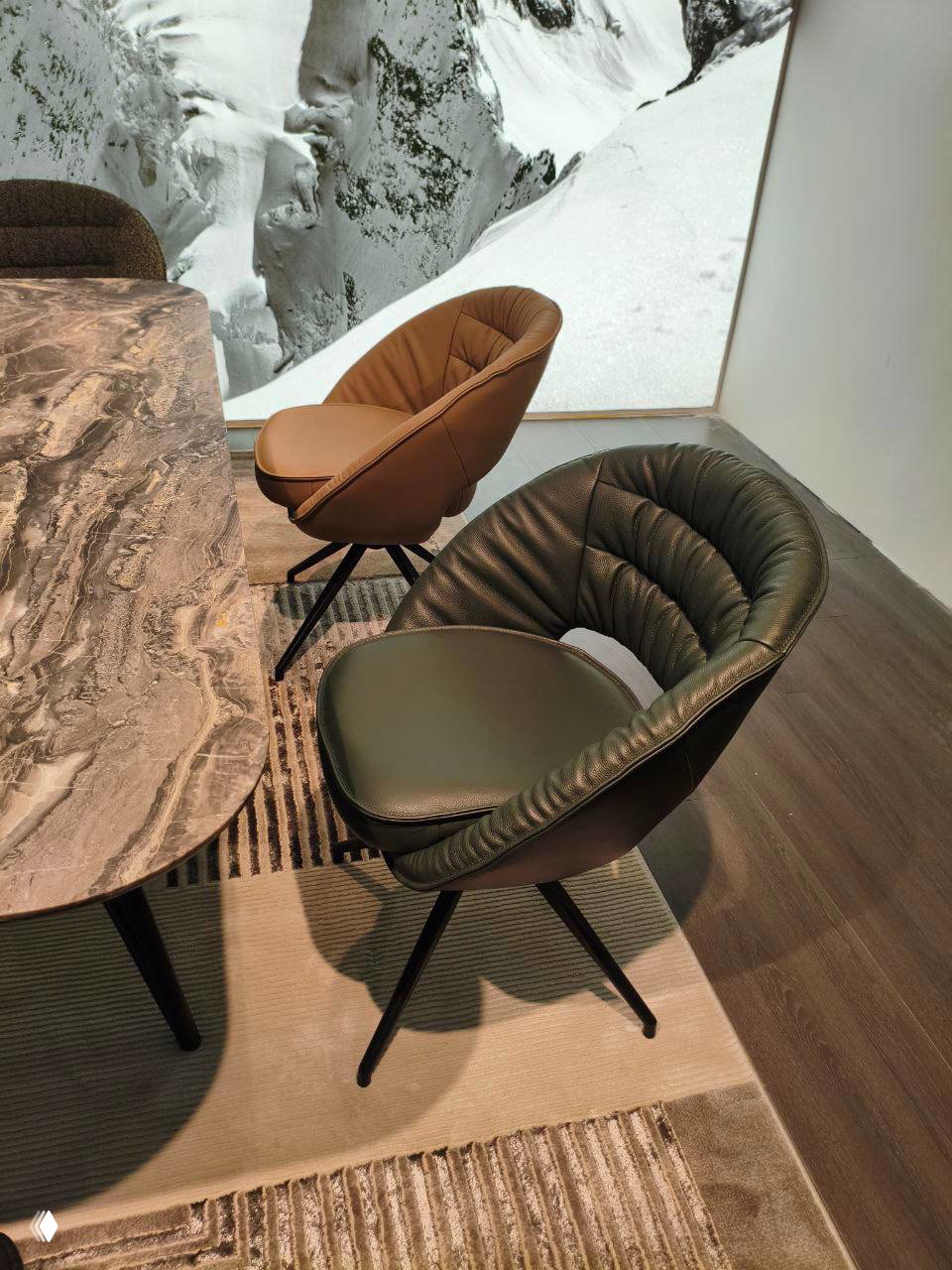 Фото: кожаные вращающиеся кресла у мраморного стола, тёмно-зелёная и карамельная обивка на фоне панно с горным пейзажем.