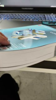 Крупный план толстого каталога CIFF в руках на фоне клавиатуры — пример полиграфии и объема материалов выставки.