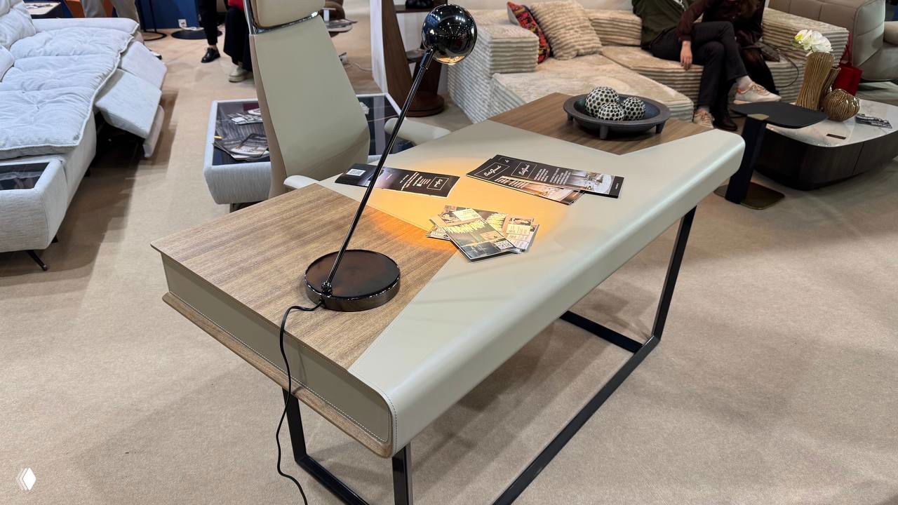 Современный стол с комбинированной столешницей, настольной лампой и разложенными рекламными материалами на выставочном стенде.