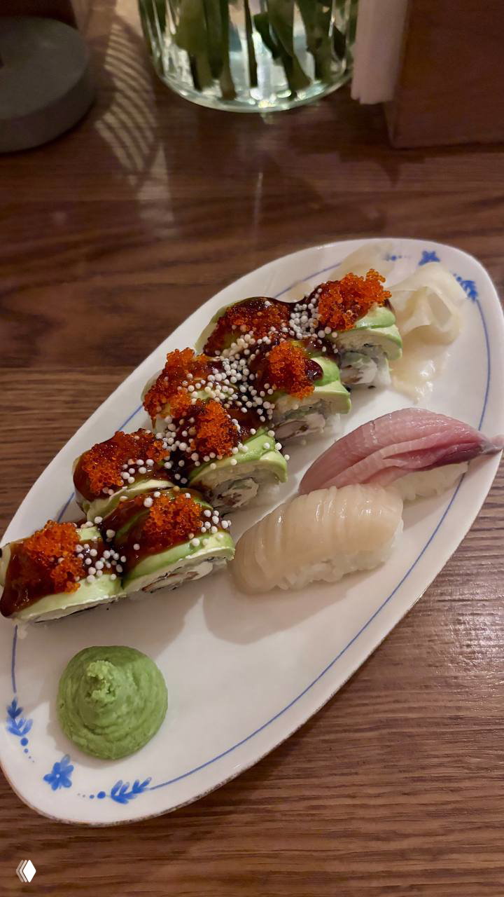 Тарелка с поп-роллами в авокадо и оранжевой икрой, рядом два нигири, порция васаби; вид на блюдо в ресторане Tokyo, детали риса и посыпок.