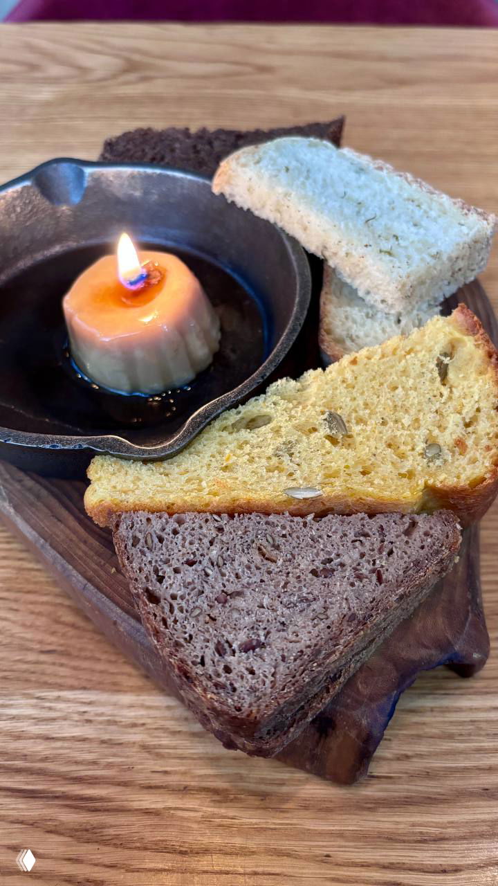 Хлебная тарелка из нескольких сортов хлеба: светлый, тёмный и тыквенный, с порцией топлёного масла-«комплимента» в мини‑сковороде и свечой.