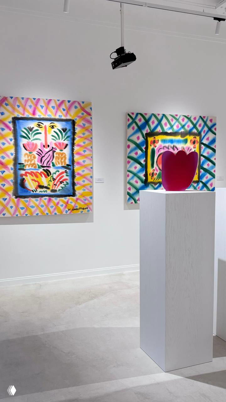 Интерьер галереи с яркими графическими картинами и небольшим розовым объектом-визуальным акцентом на постаменте.