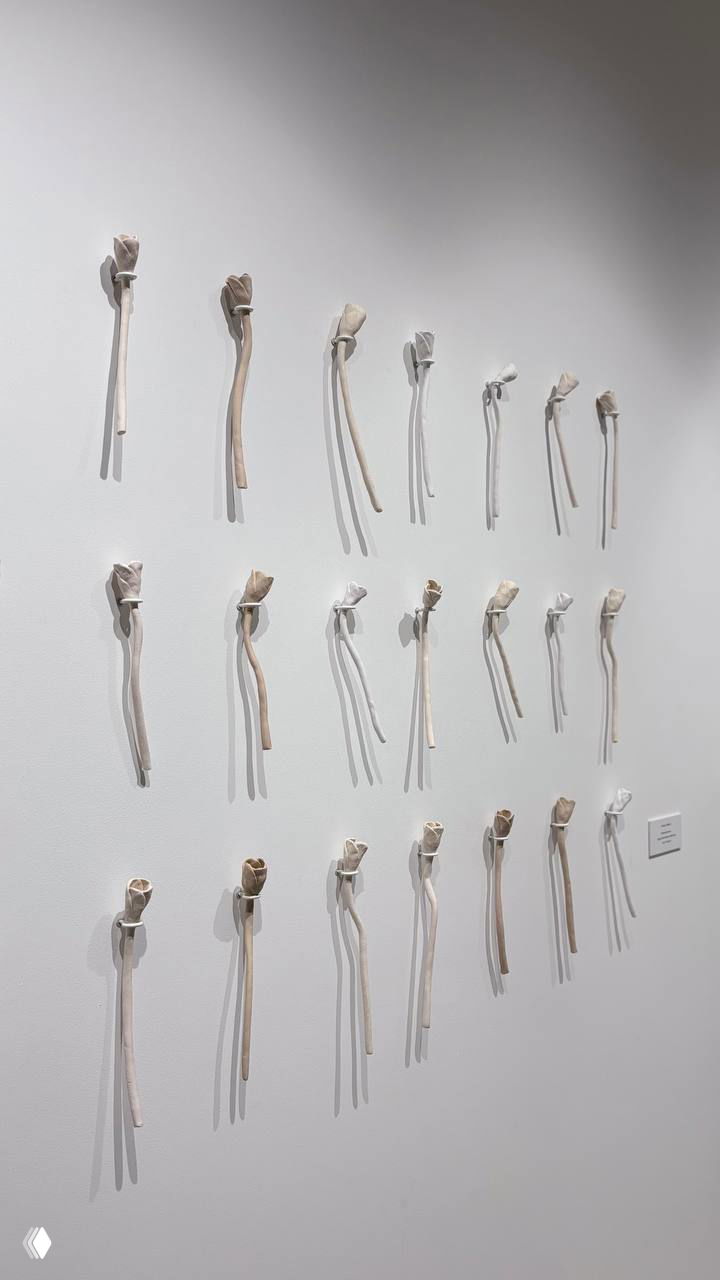 Стена с множеством небольших каменных цветков-объектов, закреплённых по сетке — серия скульптурных работ, которые продаются на выставке.