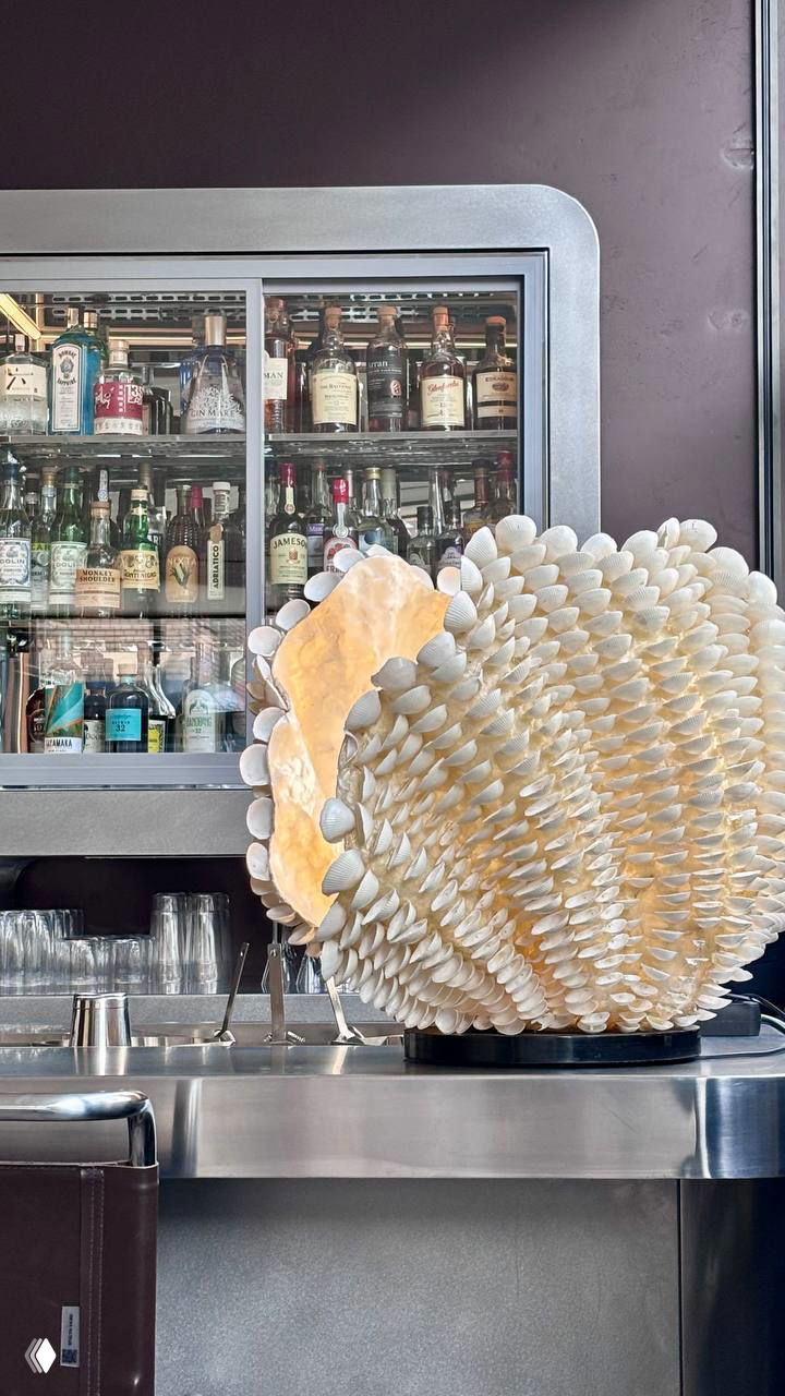 Барная стойка с витриной алкогольных напитков и декоративным крупным арт-объектом из белых раковин или пластин на переднем плане.