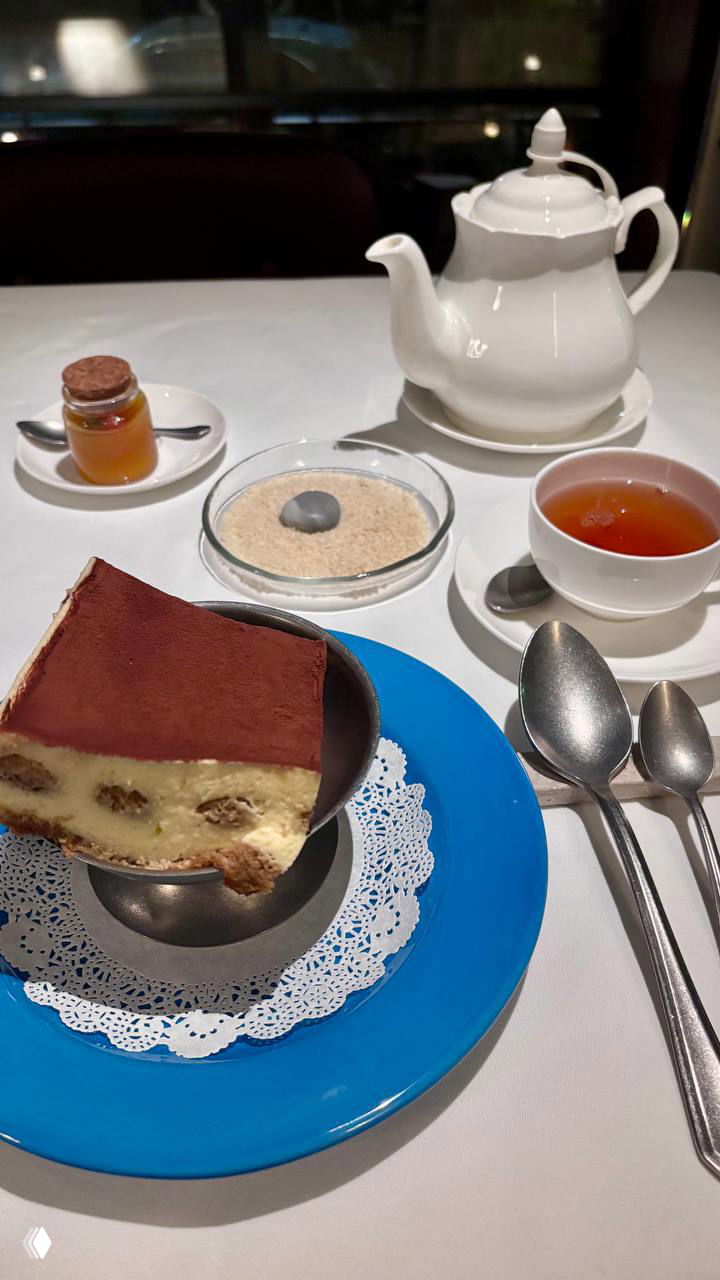 Десертная подача: тирамису на синей тарелке, чайник, чашка чая и маленькие баночки с конфитюром — сервировка перед десертом.