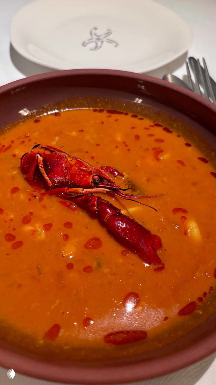 Глубокая тарелка с наваристым раковым биском оранжевого цвета, сверху лежит целая раковина рака как декоративный элемент.