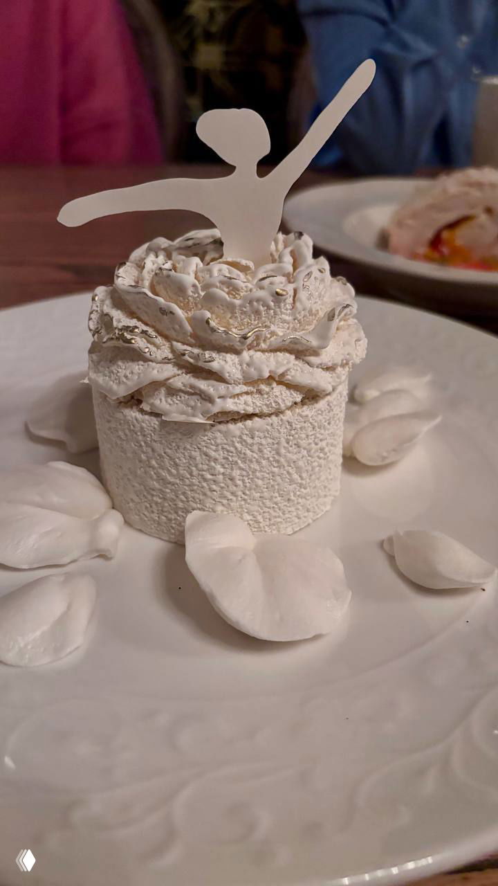 Нежный десерт в белой текстуре с крошными безе и фигуркой балерины сверху, поданная на фарфоровой тарелке