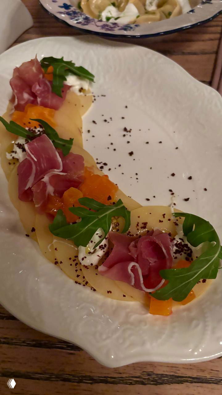 Тарелка с холодной закуской: тонко нарезанные продукты, руккола и соус, подача в изящной фарфоровой посуде на деревянном столе