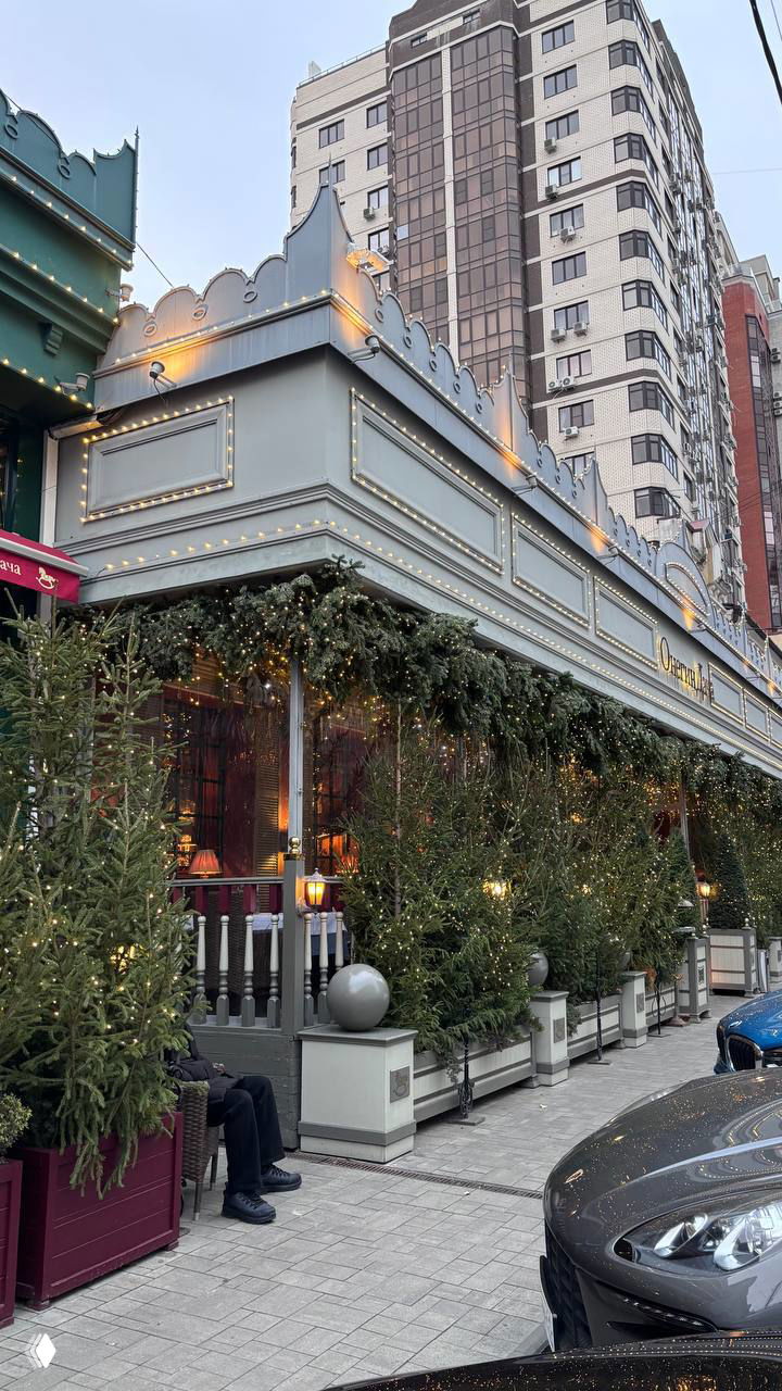 Улица и фасад ресторана Онегин Дача с уличными ёлками и подсветкой вдоль веранды на фоне жилого дома в Ростове-на-Дону