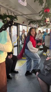 Интерьер трамвая во время представления: улыбающаяся девушка в красном шарфе, зрители аплодируют и создают тёплую праздничную атмосферу внутри салона.