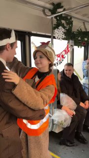 Актёры в костюмах и жилете движения исполняют сцену в проходе трамвая, зрители наблюдают и улыбаются — фрагмент иммерсивного перформанса.