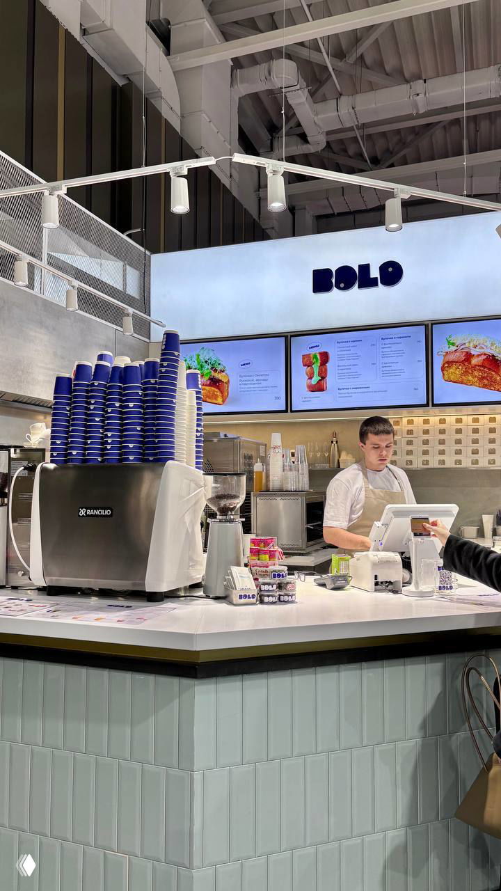 Общий вид корнера Bolo: касса, кофемашина с аккуратно сложенными синими стаканами и часть оформления заведения в современном стиле.