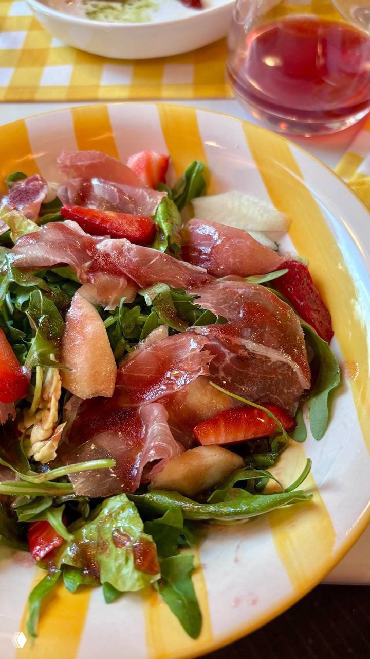 Салат с рукколой, прошутто и клубникой на яркой тарелке — свежая зелень, ягоды и тонкие ломтики прошутто под легкой заправкой.