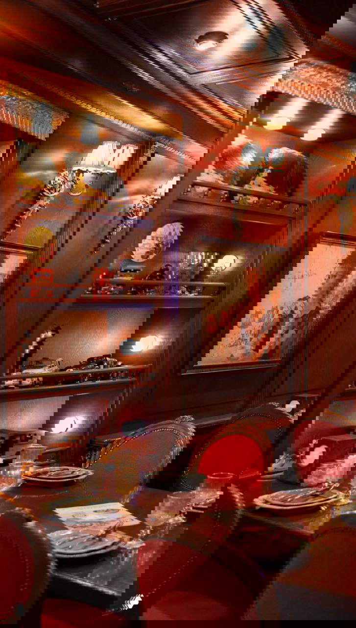 Тёплый винтажный интерьер с деревянными панелями, красными креслами и сервированными столиками, уютная атмосферная обстановка.