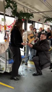 Эмоциональный момент внутри салона: музыкант с гитарой и человек на колене перед женщиной — видимо, предложение, вокруг аплодируют пассажиры.