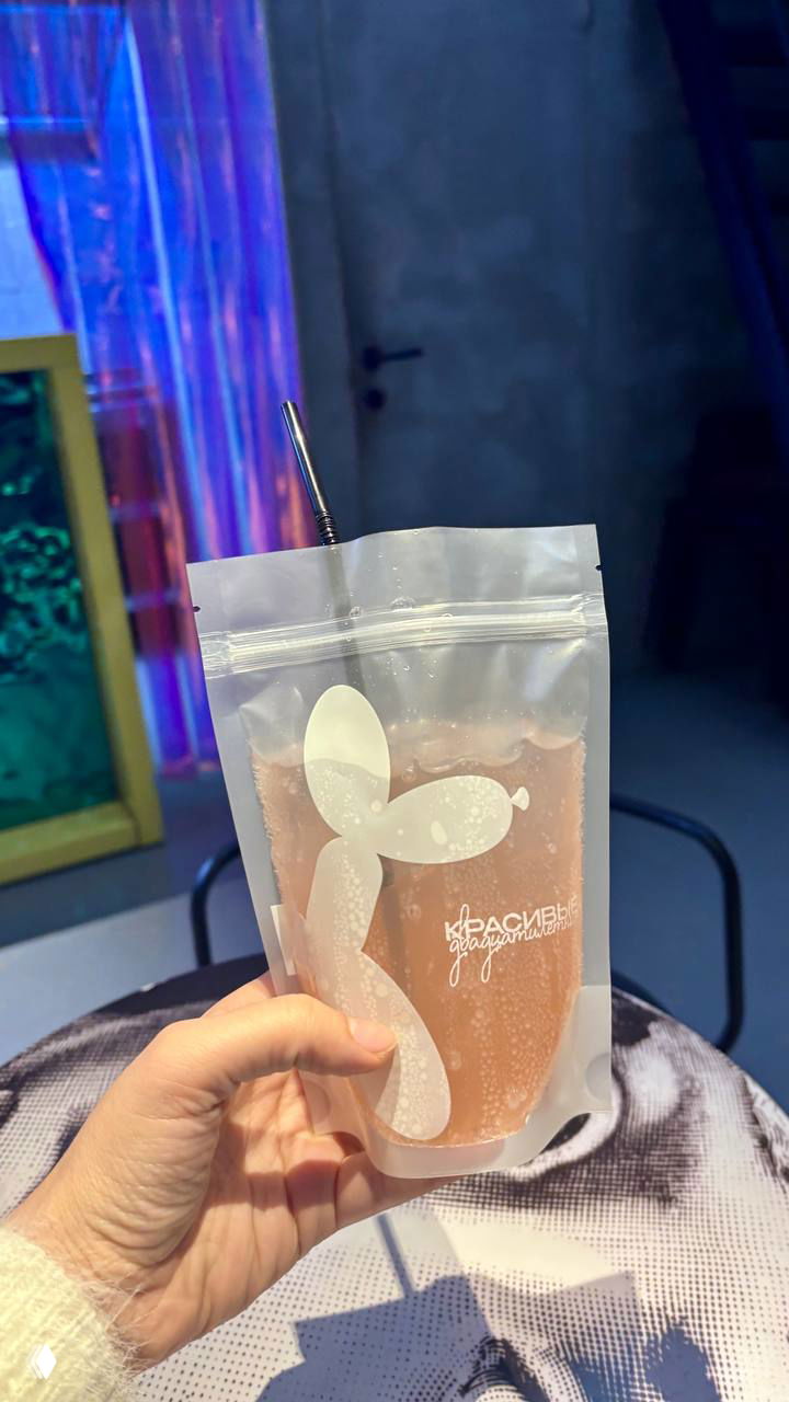 Крупный план напитка в прозрачном пакете с белым принтом шарика, рука держит пакет — фирменная подача лимонада в баре.