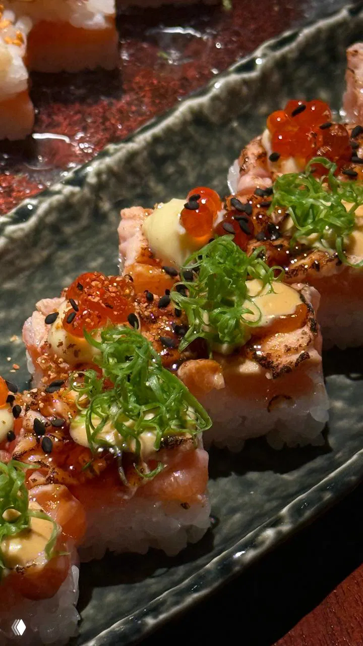 Крупный план обжаренных роллов с икрой и зеленью: кремовый соус, икорные шарики и тонко нарезанный зелёный лук сверху, аппетитная текстура.