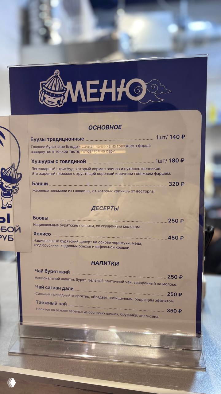 Ближний план меню заведения с разделами «Основное», «Десерты» и «Напитки», видны цены на буузы, хушууры и чай