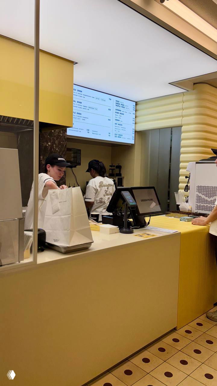 Интерьер и касса бургерной с желтыми элементами, сотрудники за прилавком и меню на экране — вид на рабочую зону ресторана Smash Point.