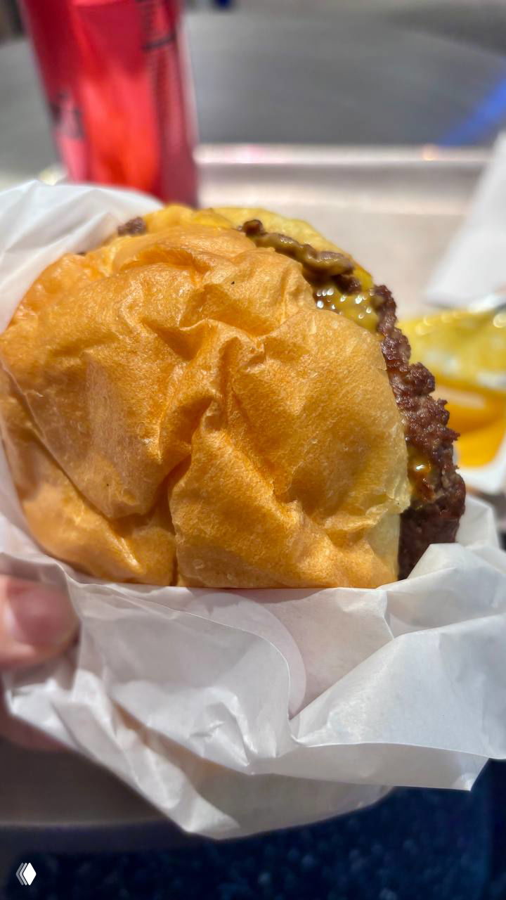 Близкий ракурс смэш-бургера на белой бумажной обертке: воздушная булочка и сочная котлета, видна расплавленная начинка и текстура булочки.