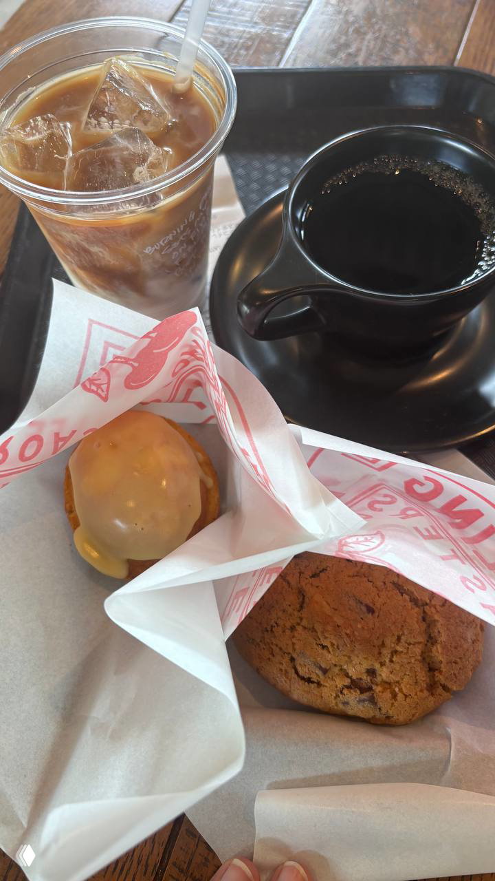 Поднос с холодным кофе в пластиковой чашке, тёмной керамической чашкой и парой печений в бумаге — повседневный заказ сети кофеен на вынос.