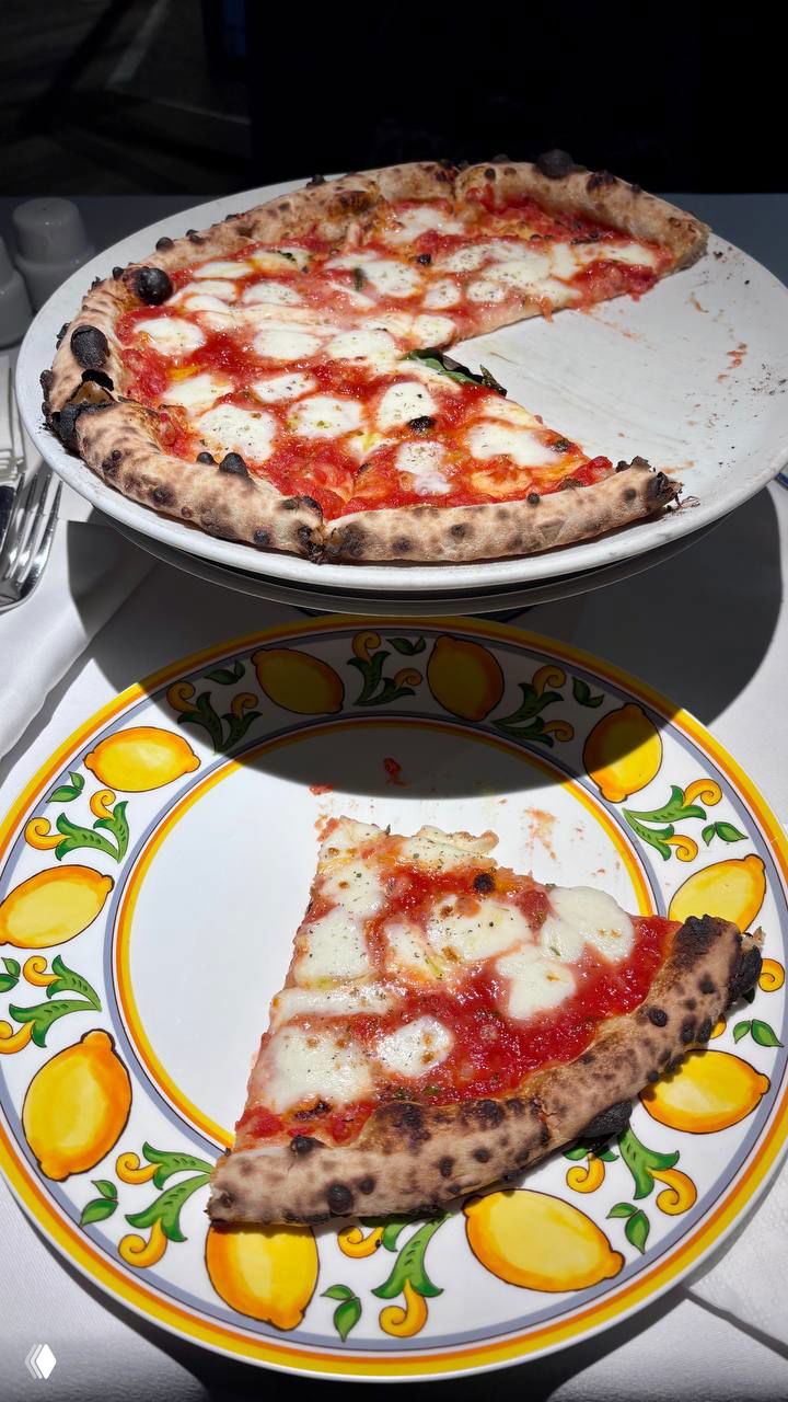 Пицца на подставке и кусок на тарелке с лимонным орнаментом в La Bottega Siciliana: видно подгоревшие точечки на корочке, расплавленный сыр и следы масла.