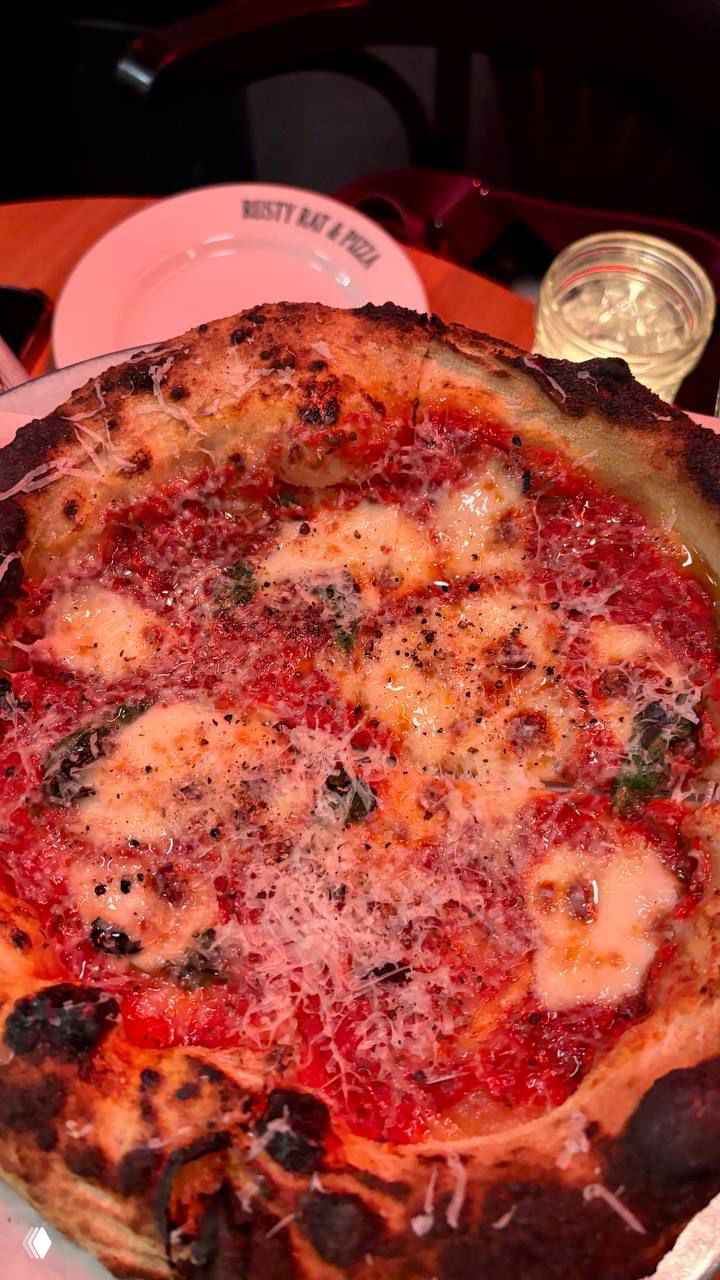 Маргарита на тарелке с подпалённым бортиком, расплавленной моцареллой и тёртым сыром — тесто выглядит воздушным и сочным.